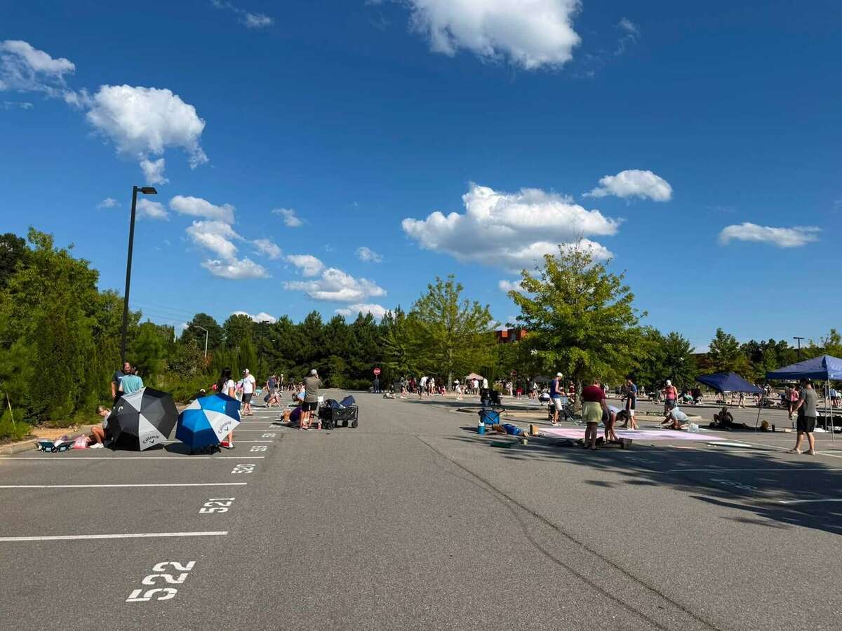 Rows of chalked parking spaces filling in across the lot under a blue sky, families working under umbrellas