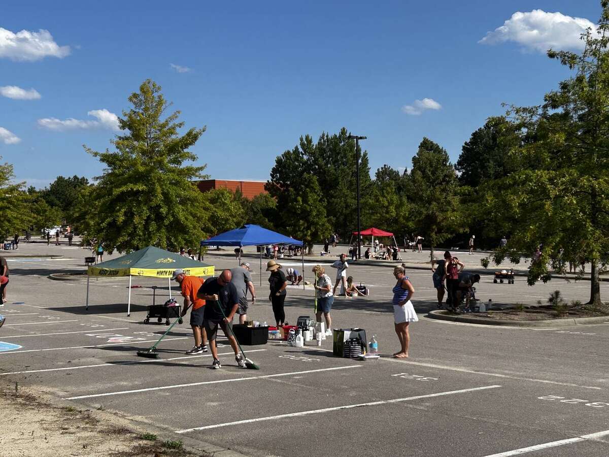 Families prepping and sweeping their parking spaces before chalking, canopies set up along the row