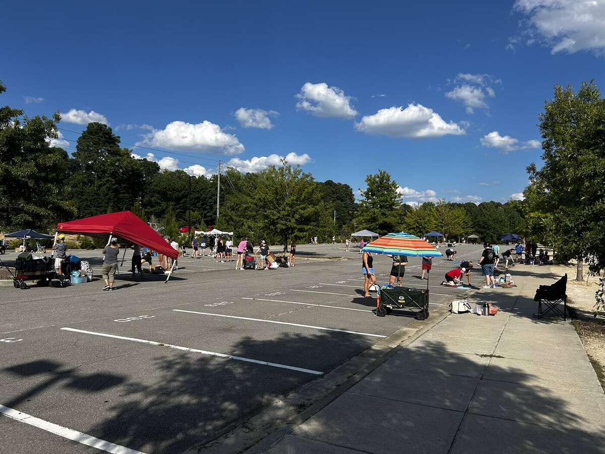 The AFHS student parking lot on chalk night - canopies and umbrellas set up across the lot under a clear blue sky, families decorating spaces