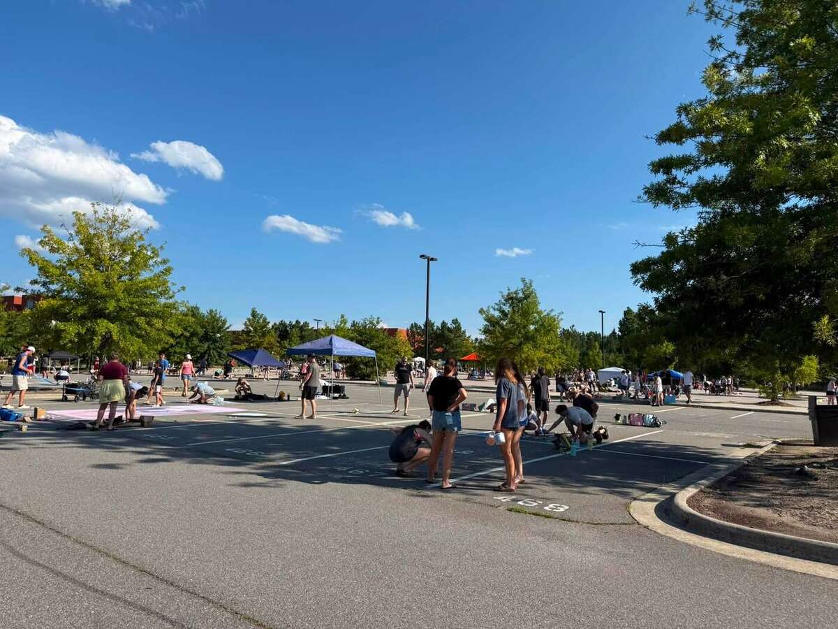 Families spread out across the student lot, bent over their parking spaces with canopies and chalk supplies around them