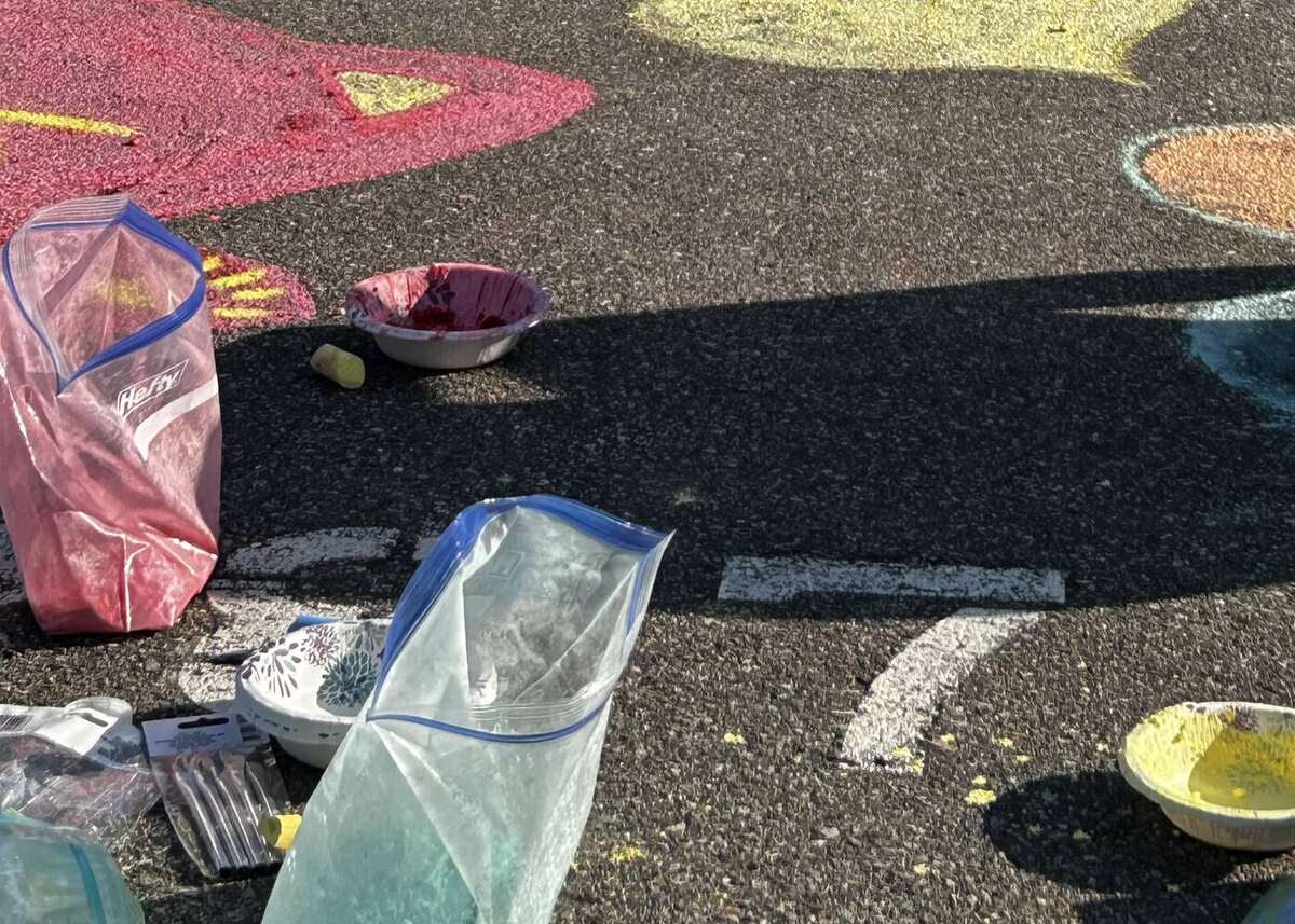 Chalk supplies on the pavement - bags of ground chalk, bowls of chalk mixed with water, and the finished artwork around them