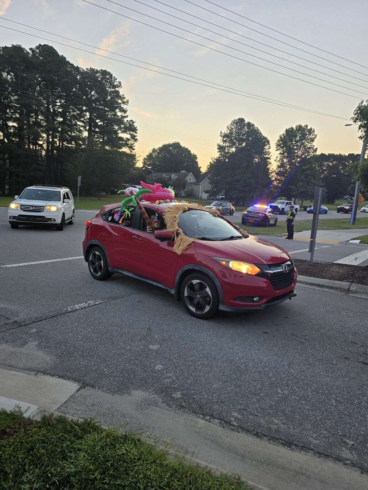 A red SUV decorated with an inflatable flamingo, a palm tree and a grass skirt along the roofline