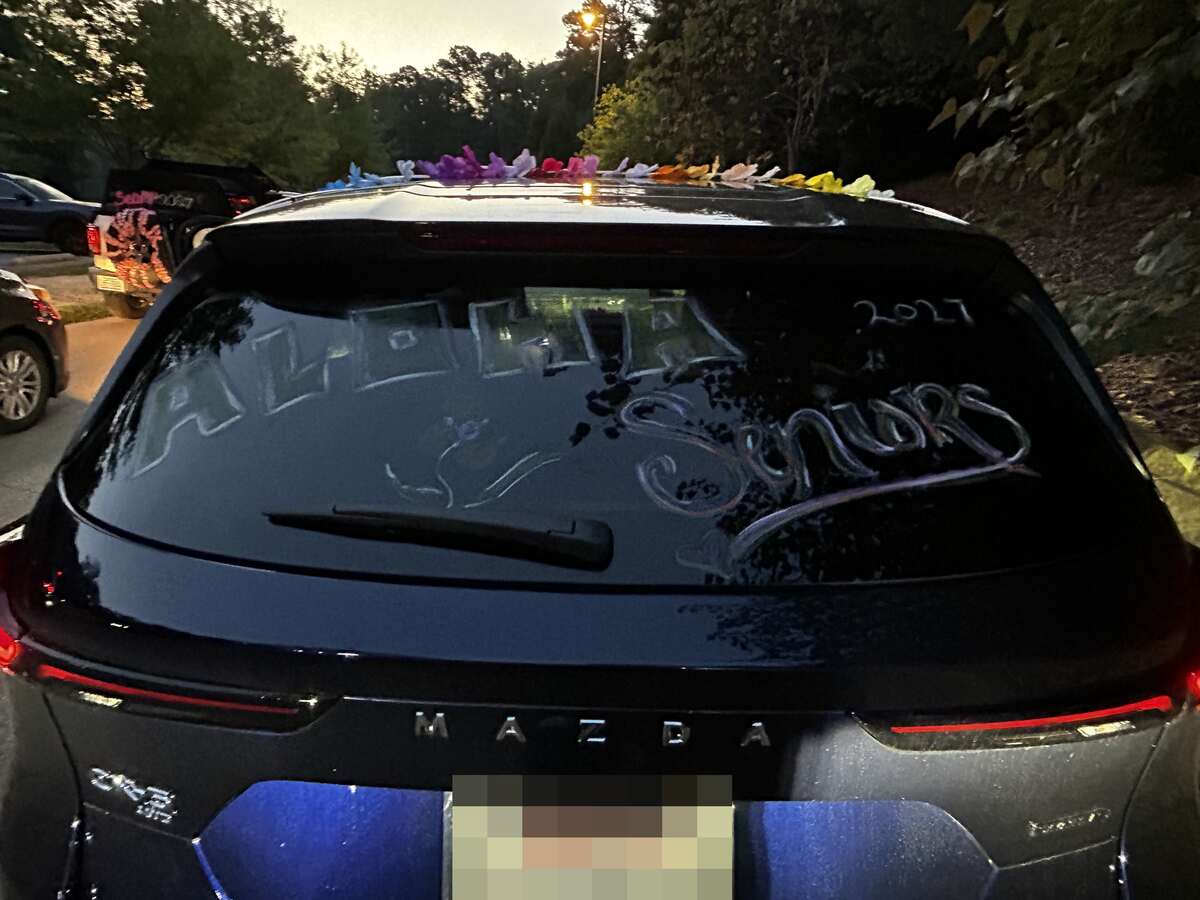 ALOHA Seniors 2027 written across a rear window, with leis strung along the roofline, before dawn