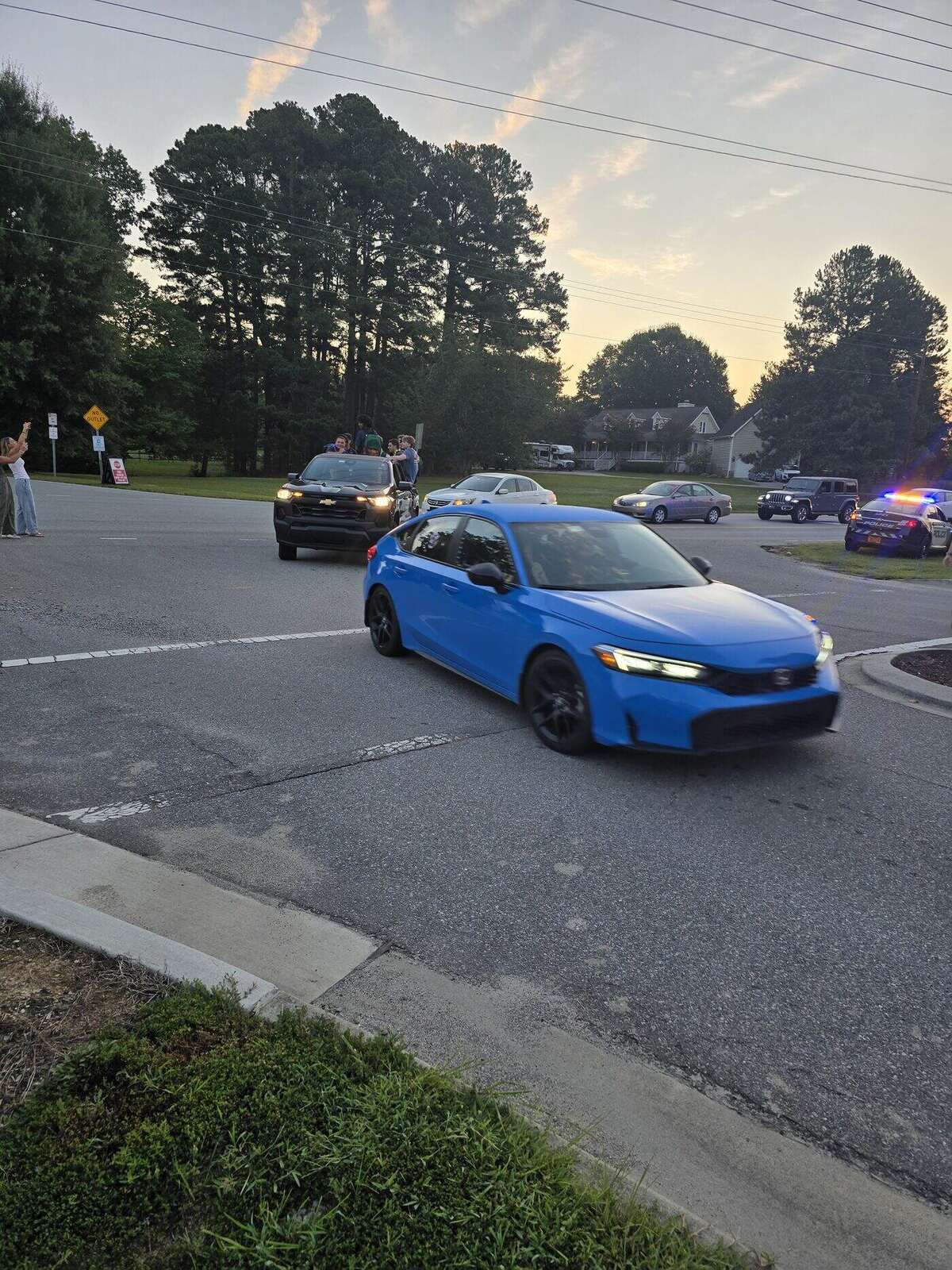 A decorated senior car heading toward school with the sunrise behind the treeline