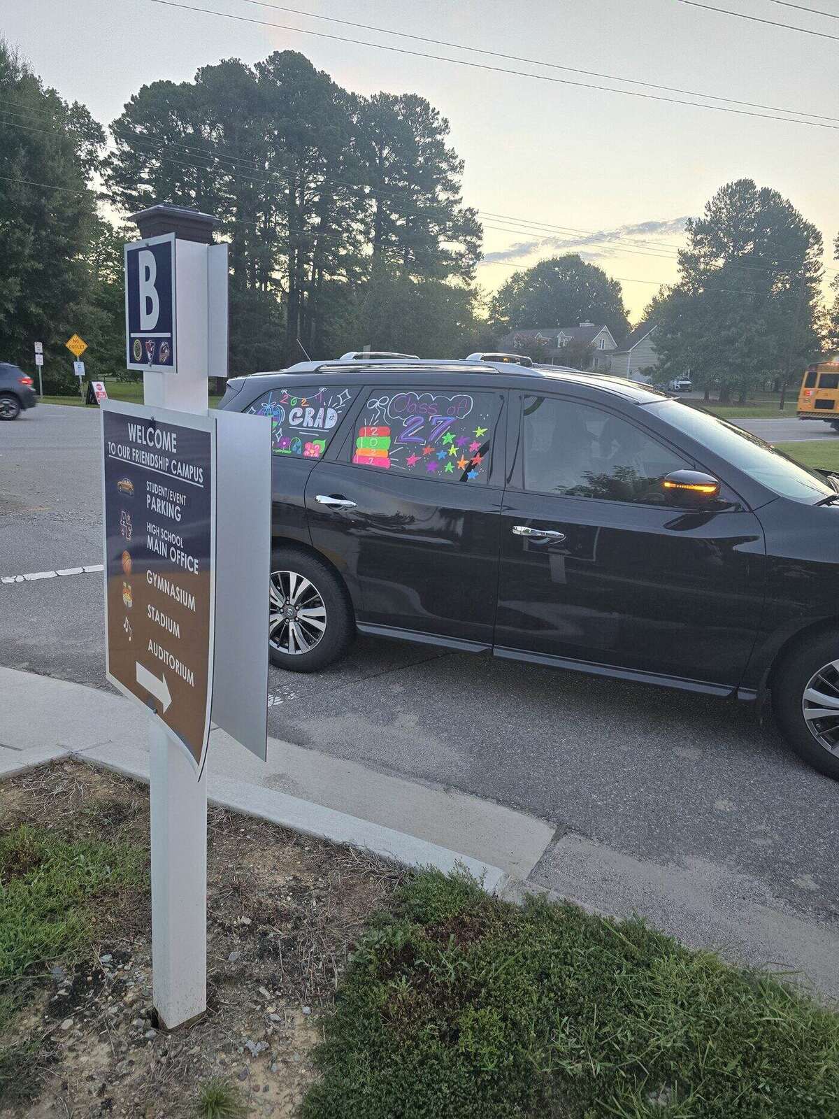 A senior's SUV with GRAD and 27 painted on the windows, pulling past the Apex Friendship campus welcome sign