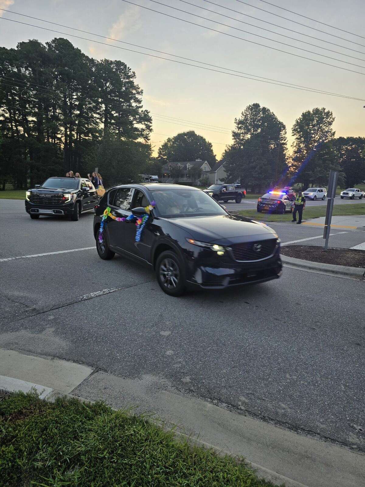 A dark SUV trimmed with leis and paper flowers moving through the intersection