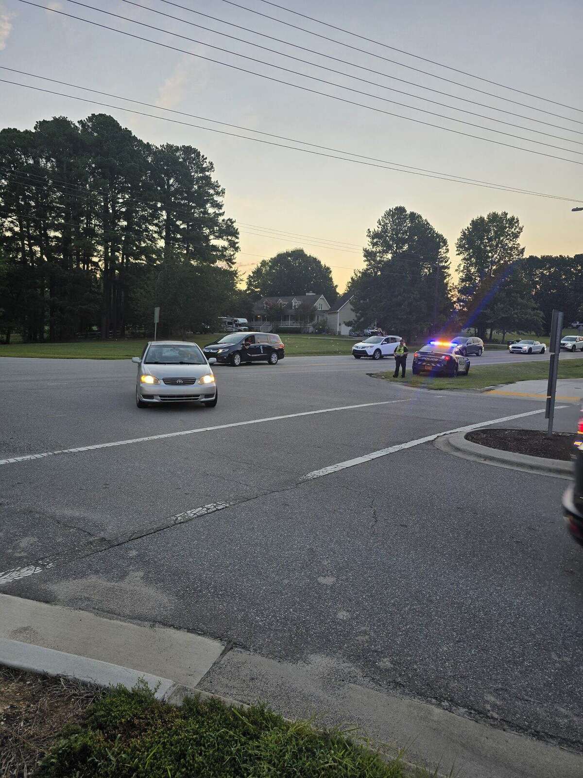 An Apex Police officer directing traffic at the intersection as the parade rolls through, patrol cars with lights running