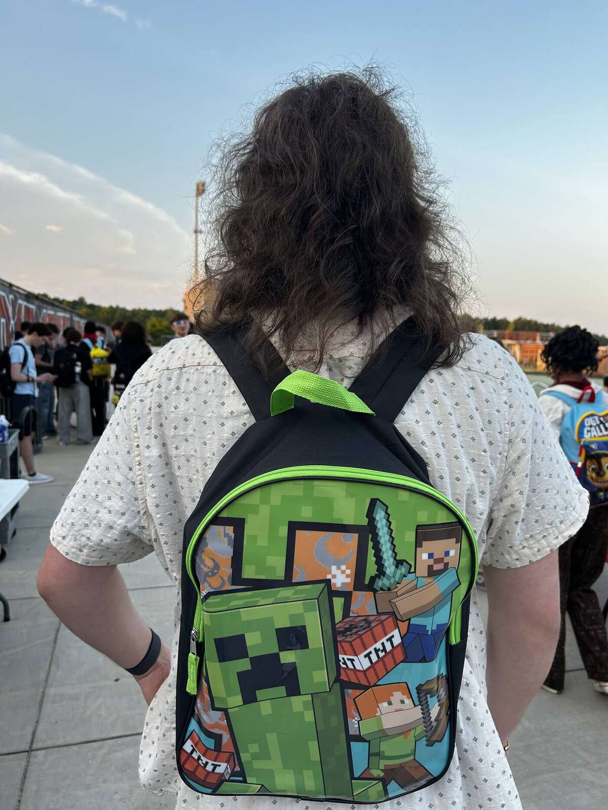 A senior at Sunrise wearing a child-sized Minecraft backpack, seen from behind