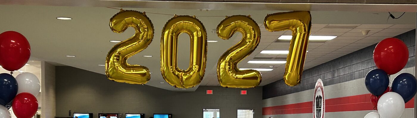 Gold 2027 balloons hanging over the AFHS cafeteria, with red, white and blue balloon clusters below
