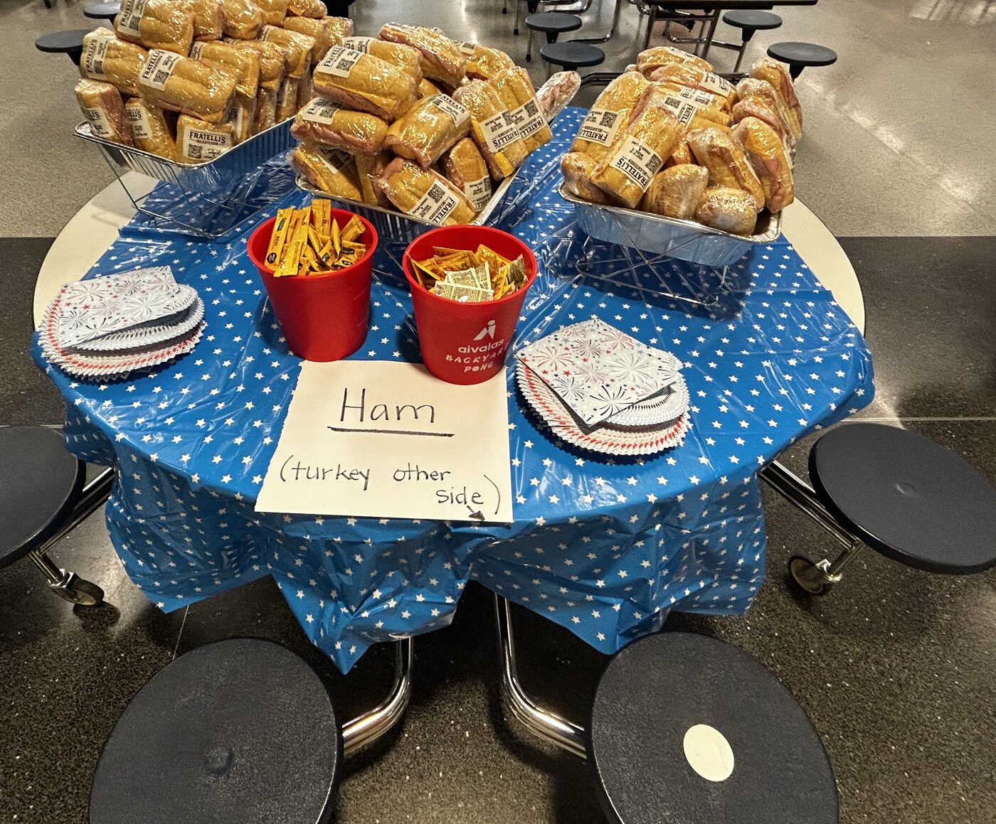 The ham table, with trays of wrapped sandwiches, condiment cups and a sign reading Ham, turkey other side