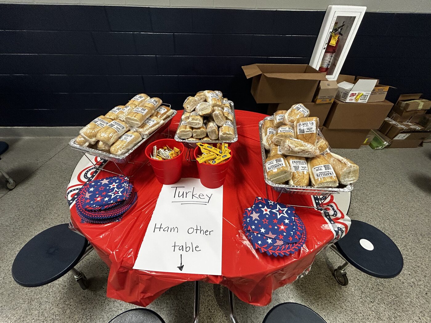 Trays of wrapped Fratelli's turkey sandwiches on a red-draped cafeteria table, with a hand-lettered Turkey sign