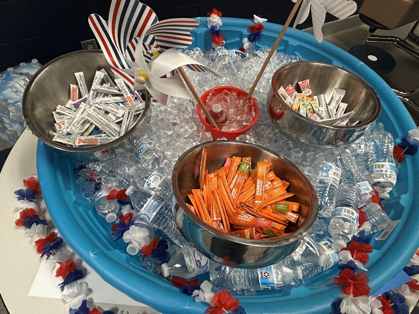 A kiddie pool packed with iced bottled water, bowls of drink flavor packets and patriotic pinwheels